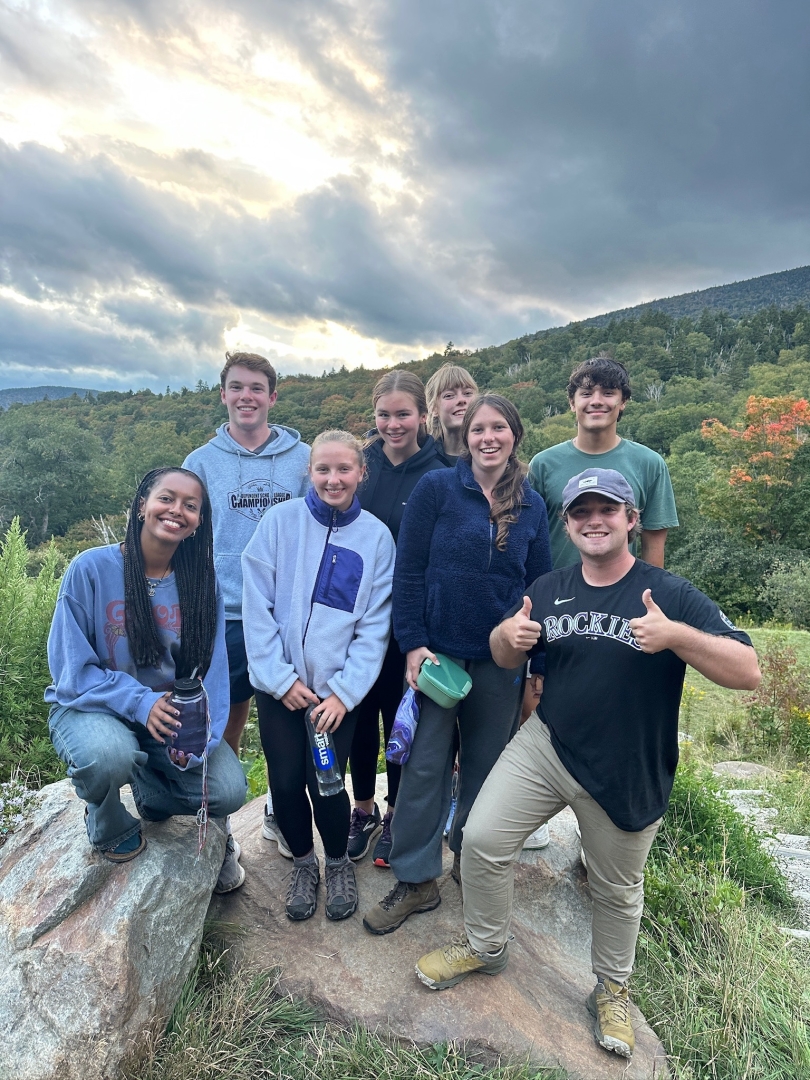 a group of eight people standing on rocks, smiling. In the background are trees on a mountain