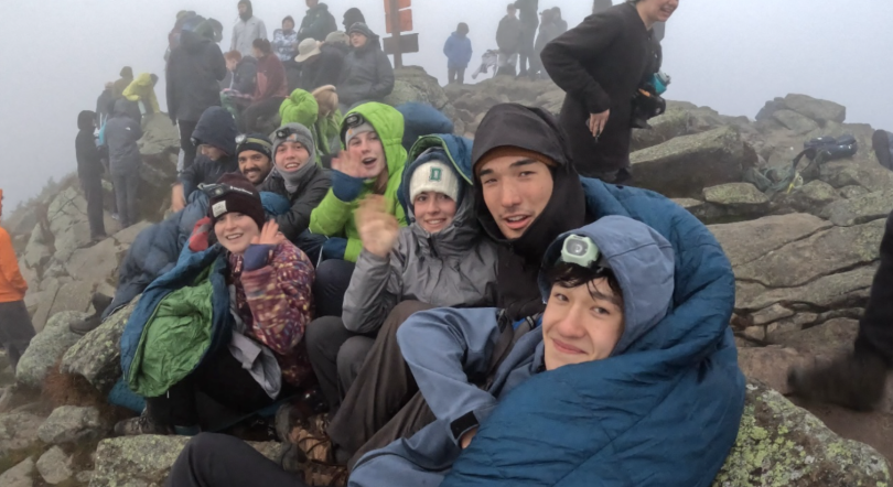 A group of first-years huddling together to warm up at the summit. 