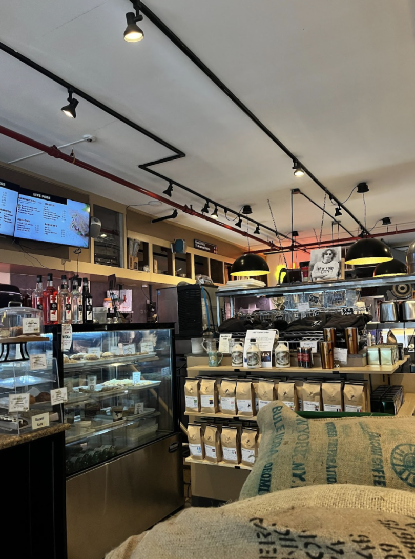 The interior of Dirt Cowboy. There is a counter and a display case with pastries, along with bags of coffee, mugs, and syrup for sale.