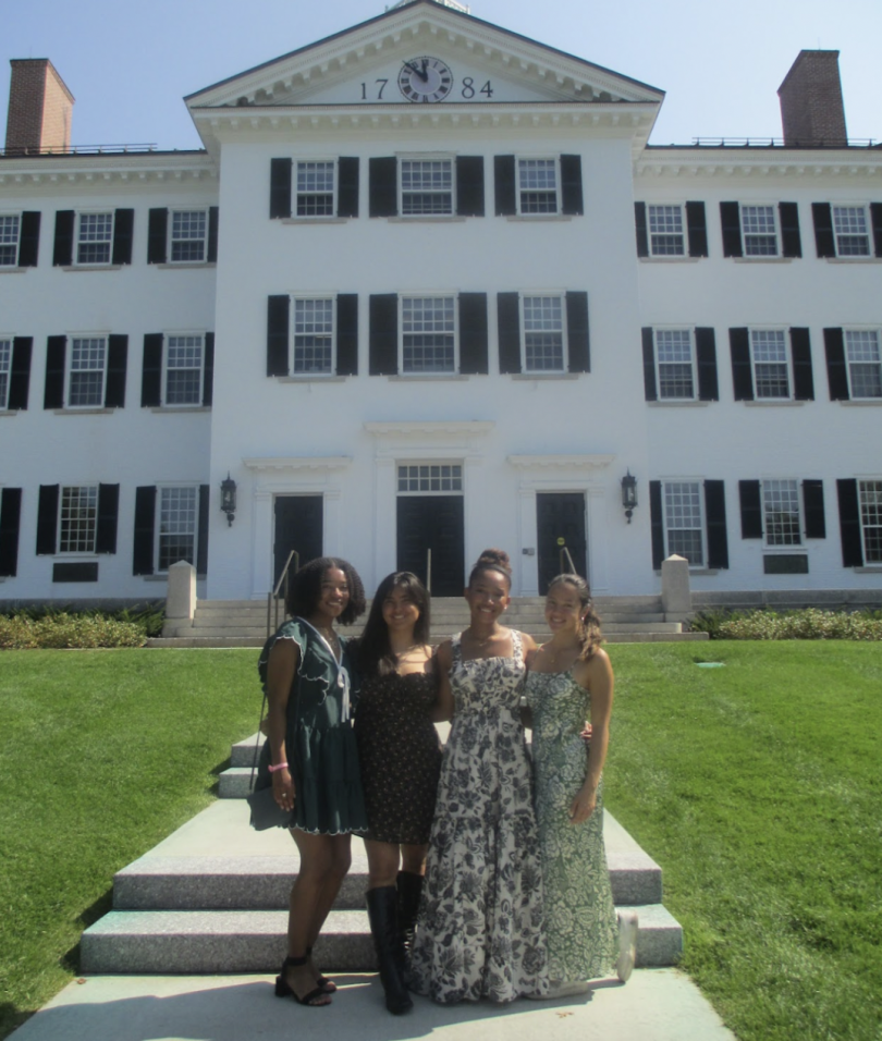 4 girls in dresses pose in front of Dartmouth Hall, a 3-storey building with green shutters and windows 