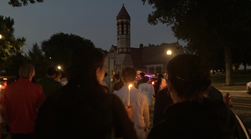 A crowd of '28s holding lit candles walk for the twilight ceremony, with rollins chapel in the dim background