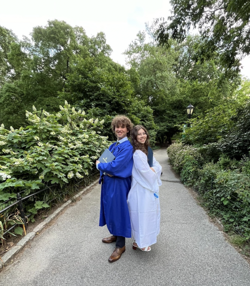 Serena and her brother stand back to back holding their diplomas. They are smiling and are standing in the middle of the sidewalk with trees all around. 