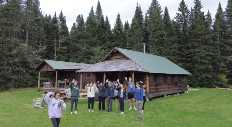 Students standing outside a cabin waving