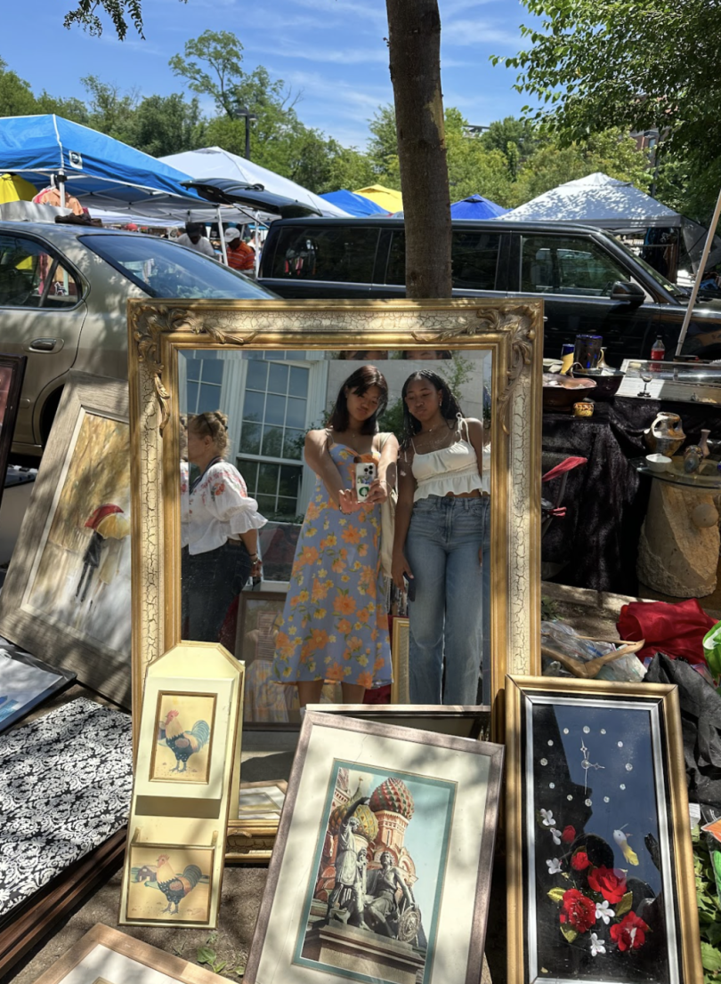 Two girls posing in front of a mirror surrounded by an array of eccentric picture frames outside.