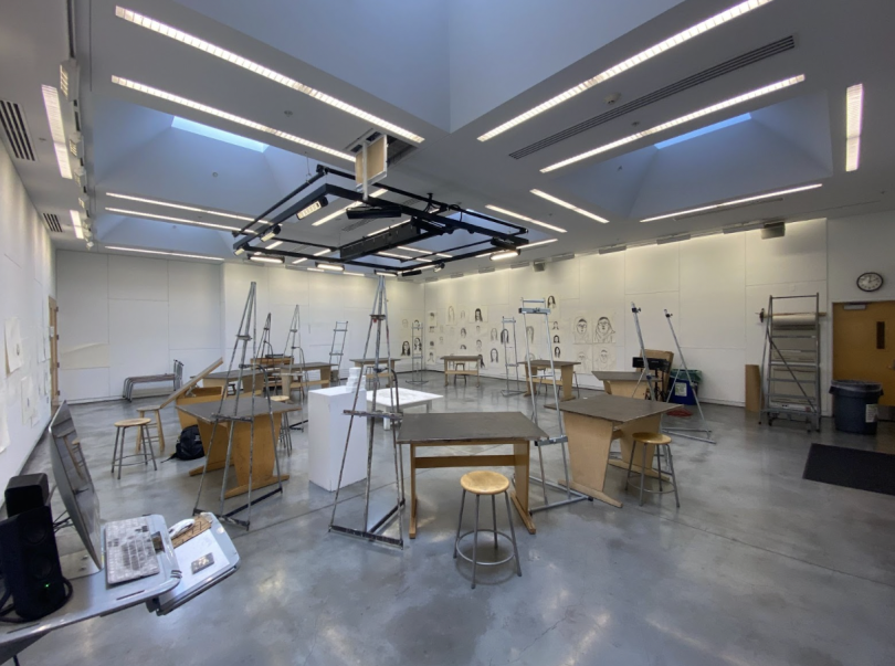 A brightly lit art studio containing a circle of desks and easels.