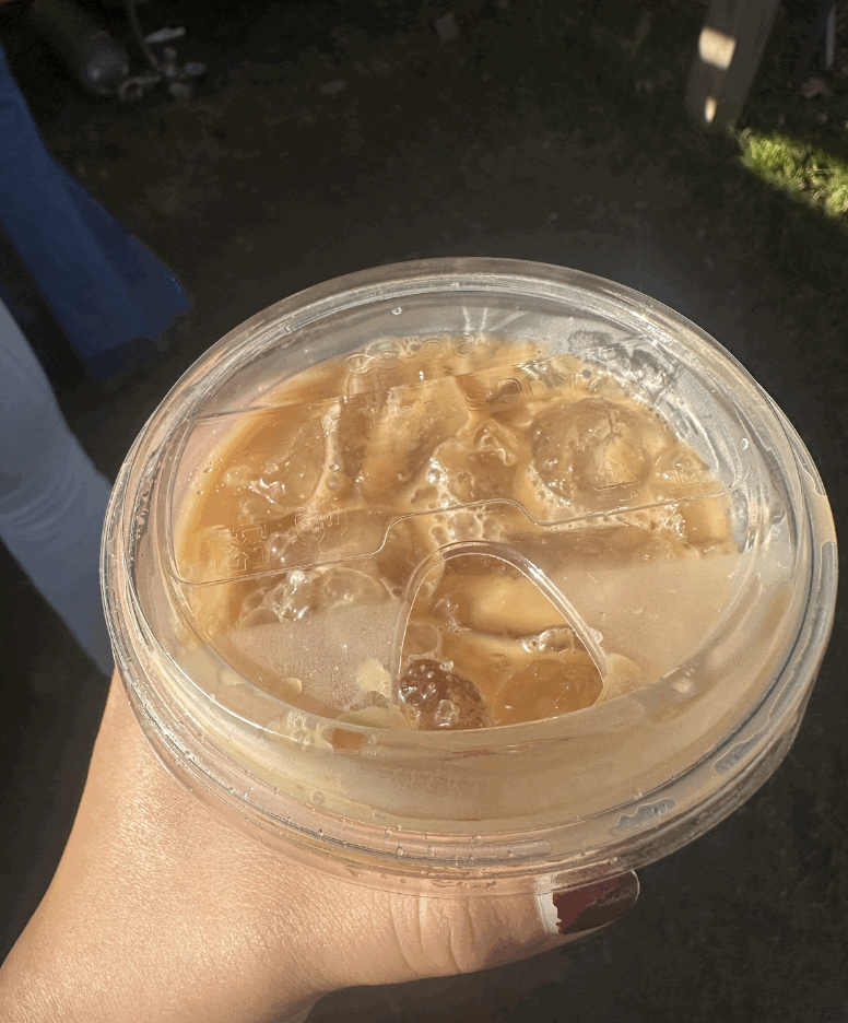 An image of me, Crystal, holding a plastic cup with a lid containing a Horchattie, an oat milk latte, and ice. The background is plain.