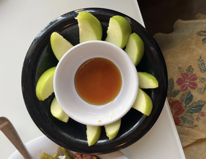 a small white dish with orange honey inside of it is sitting in a black bowl with green apples in a circle around the small white dish. 
