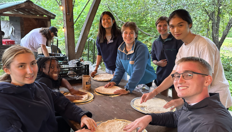 My trip group circles around a table, where we are stretching pizza dough over pans.