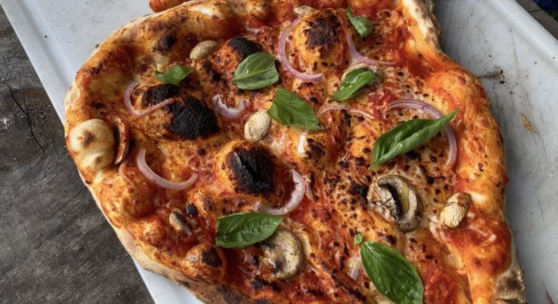 A close up shot of a pizza we made. This one is topped with red onion, mushrooms, and fresh basil leaves.
