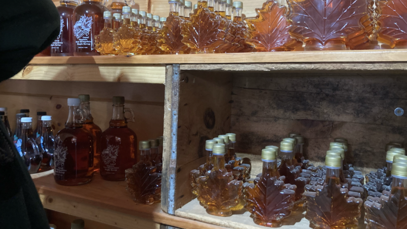 A two-tiered shelf, both shelves filled with maple-leaf shaped bottles of syrup and larger jugs
