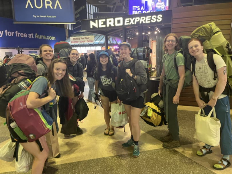 Seven Dartmouth students smile for a photo in Boston's South Station. They are all carrying many bags, and look like they are ready for a hike.
