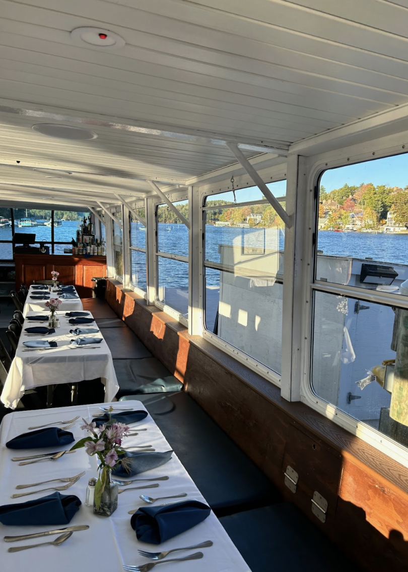 the inside of a boat, tables are set, water is in the background