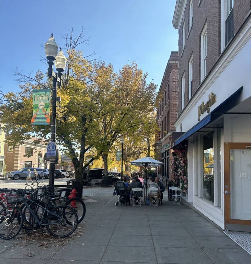 A picture looking down the sidewalk on Main Street. There are bikes parked on the left, trees in the background, and chairs/tables on the sidewalk.