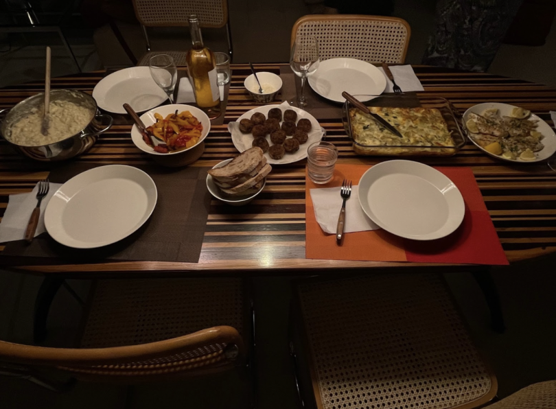 A wooden, striped table sits in the image with empty chairs around it. On top, there are plates in front of each chair with five different dishes in the middle.