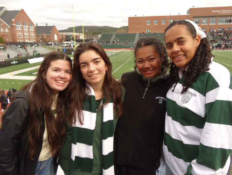 Four girls posing for a photograph in front of a football field.