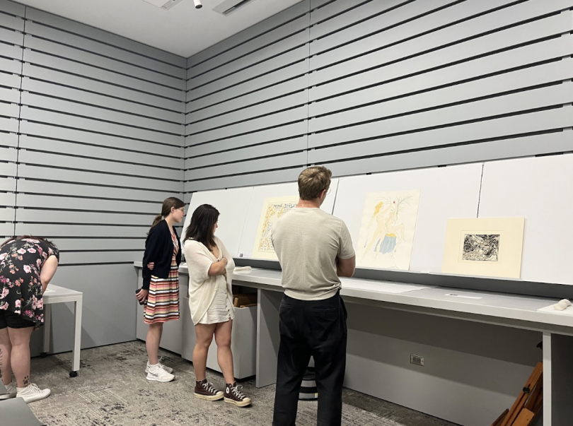 Four figures stand inside a room looking at pieces of art on the walls.