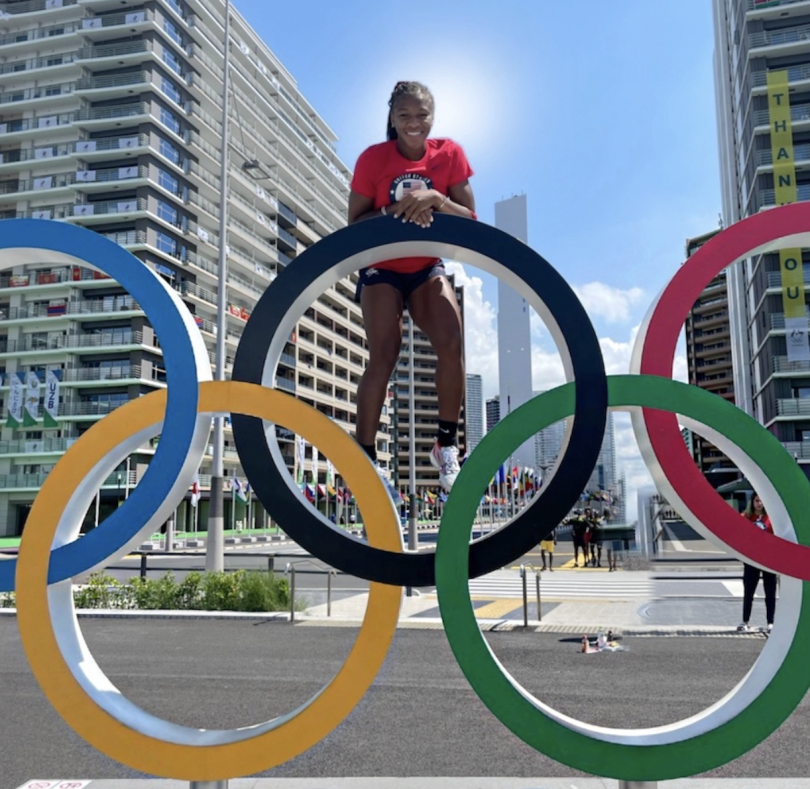 A woman stands on a large Olympic Ring setup with bright blue skies