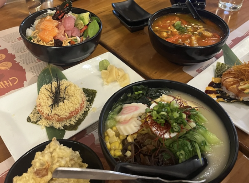 An image of food on a table at an East Asian Restaurant. The table has bowls of ramen and a sushi donut.
