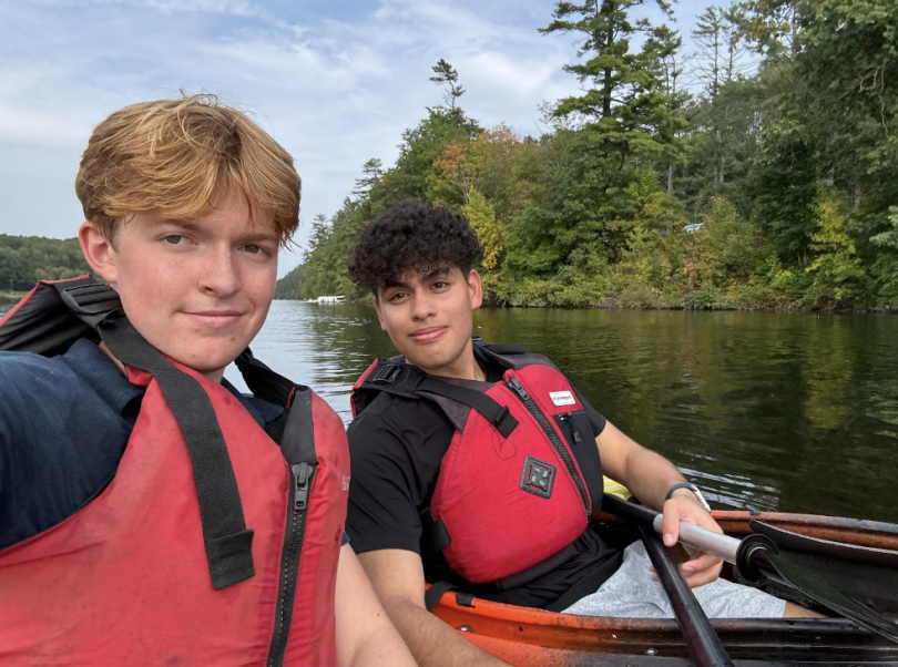 Picture of me and my friend August in the middle of the Connecticut River in our Kayaks. We're both posing for a selfie with several trees in the background.