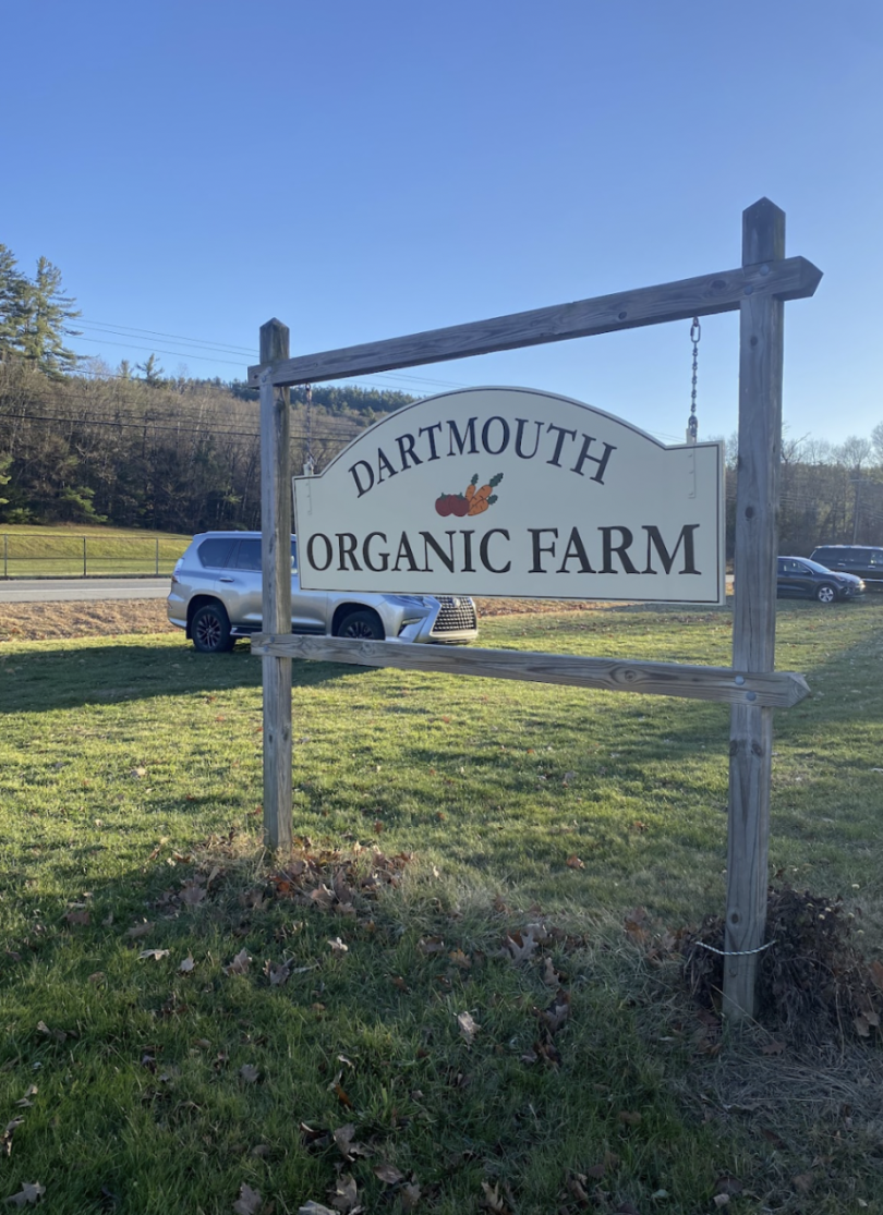 Wooden sign in the grass that reads "Dartmouth Organic Farm" with trees in the background