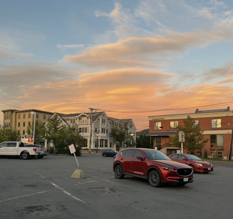 A sunset with numerous buildings under it and a parking lot.