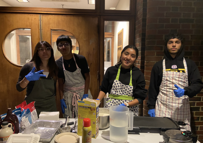 Four students posing in front of a brick building cooking pancakes!