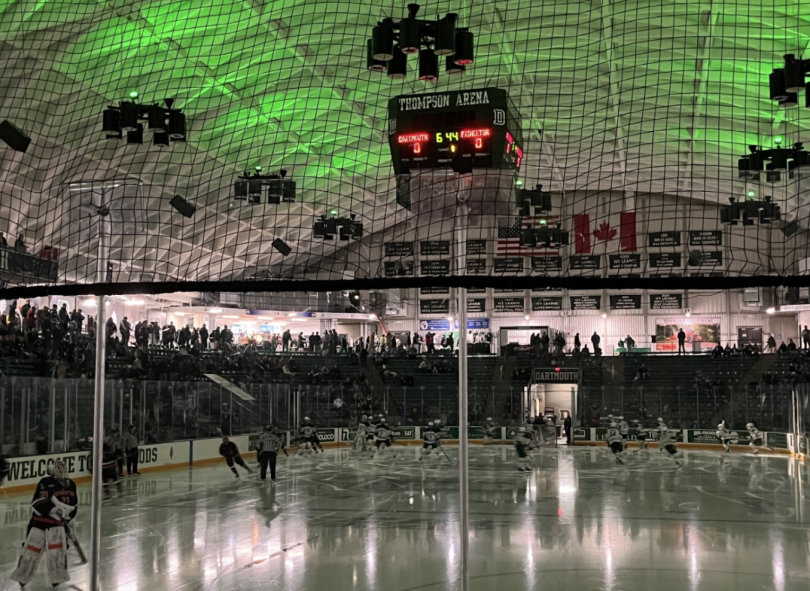 An ice rink filled with male hockey players. The ceiling glows with green lights.