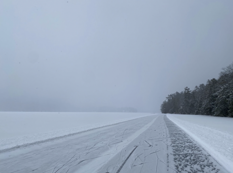 A cleared path on the lake with clouds of snow obscuring the horizon.
