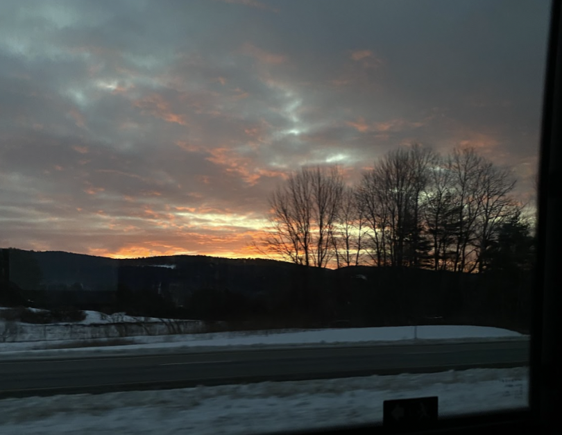 Winter sunrise with silhouetted trees, snowy roadside, and an orange and pink horizon.