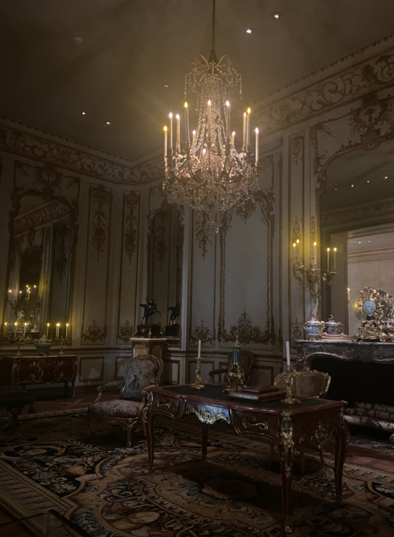 An opulent room with intricate gilded moldings, a grand crystal chandelier, antique furniture, and candle-lit ambiance.