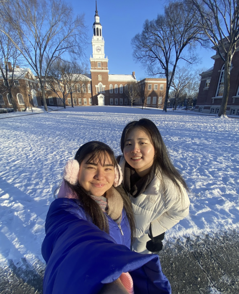 Two friends smile for a selfie in front of Baker Tower. Snow covers the ground.