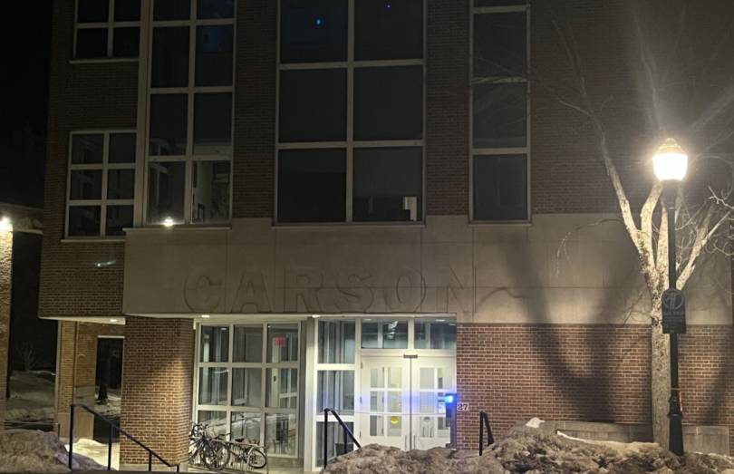 A brick building with the word "Carson" above a glass doorway. It is night time and a street light shines.