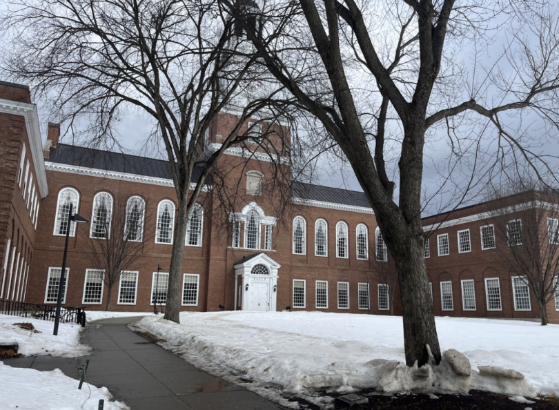 A huge brick building with a snowy lawn in front of it. There are three trees on the lawn.