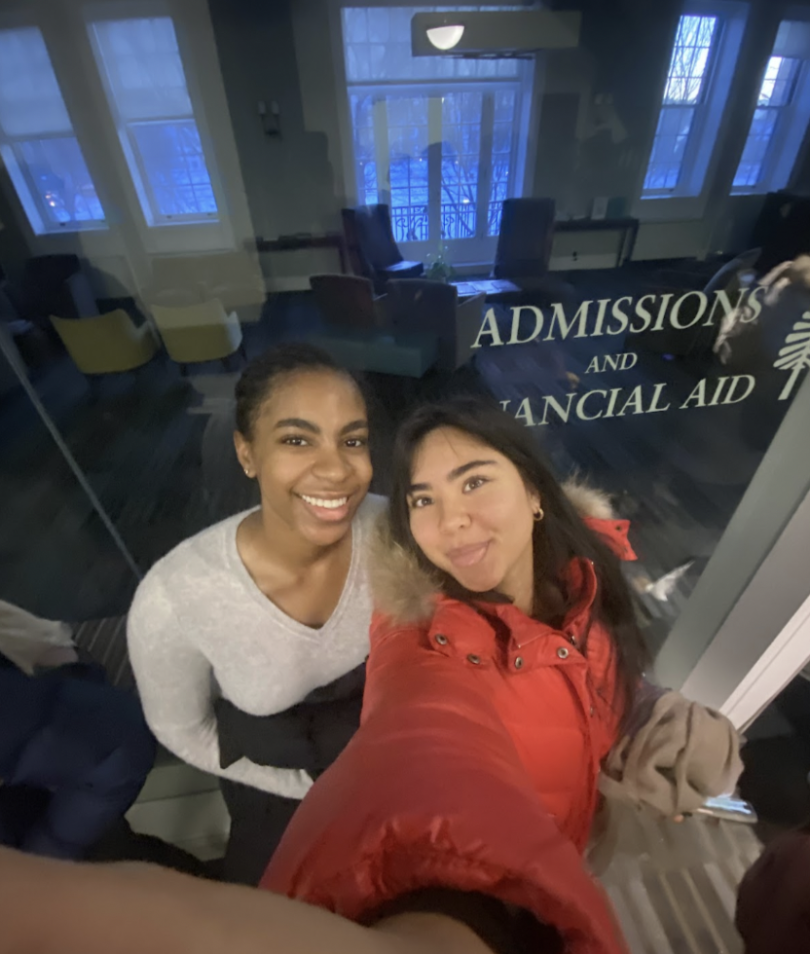 A selfie of two young women standing in front of a glass door with a sign that reads "ADMISSIONS AND FINANCIAL AID."