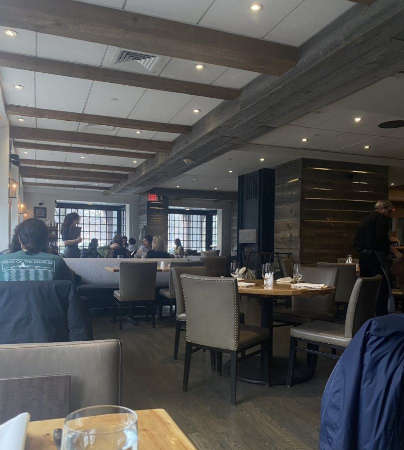 Interior of "PINE" restaurant featuring wooden beams, rustic décor, and a warm ambiance with diners seated at tables and a waiter attending to guests.