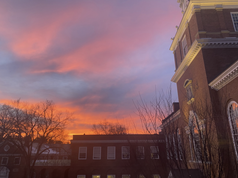 A vibrant sunset paints the sky in hues of pink, purple, and orange, casting a warm glow on Baker Library