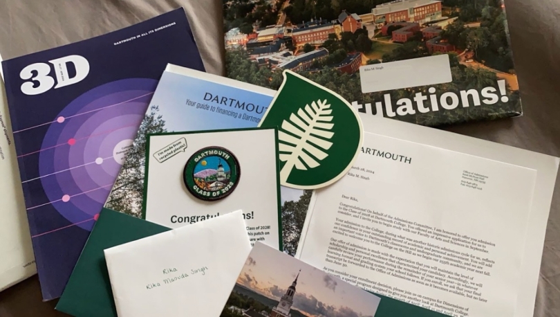 A variety of papers are shown, including a "3D" Dartmouth Magazine, an acceptance letter, a Dartmouth-themed patch, and a large sticker of the Dartmouth logo.