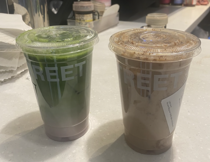 Two clear cups sit on a countertop. The left cup contains a vibrant green iced Matcha drink, layered with a light pink base, while the right cup holds a creamy, light brown beverage topped with a rich froth. Both cups are branded with the word "STREET."