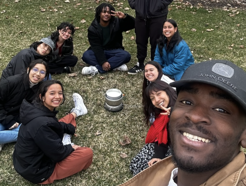 An image of students sitting in a circle on a lawn with a pot of milk in the middle