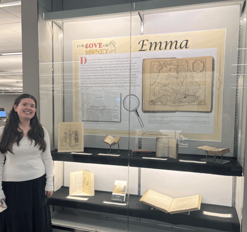 A girl with brown hair wearing a white top and blue skirt stands in front of a glass case with a poster that reads "For Love or Money."