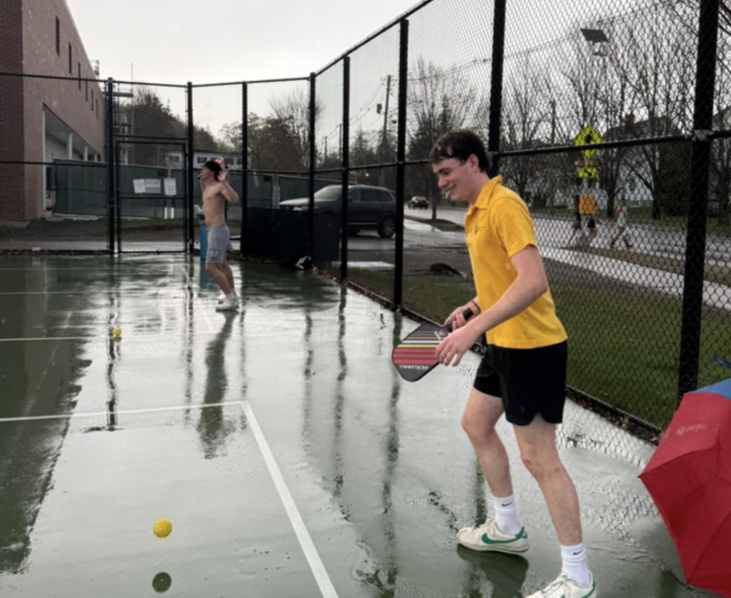 A person in a bright yellow shirt in the middle of returning a yellow plastic ball that just bounced off the ground