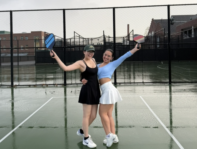 Two students side-hugging each other while raising their paddles to celebrate a victory!