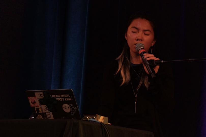 A student closes their eyes, singing into a microphone. In front of them is a laptop on a table.