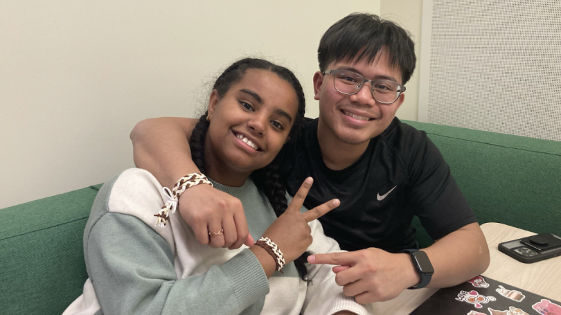 Two students smiling. Both students are wearing handmade brown and white braided bracelets.
