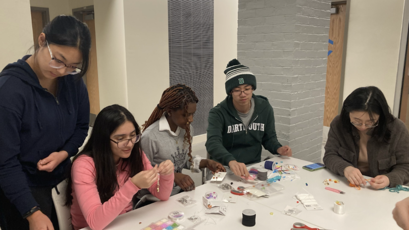Students sit around a table, crafting. The table is covered in beads, charms, and tools.