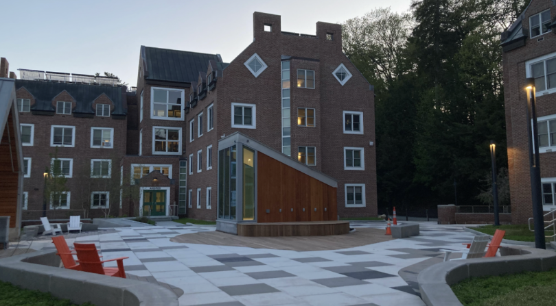 A side view of the Brace Commons rooftop. In the center of the image is a trapezoidal structure made of glass and wood. There is a short wooden platform attached to the structure's side. To the image's far left is Andres Hall and to the right is Zimmerma