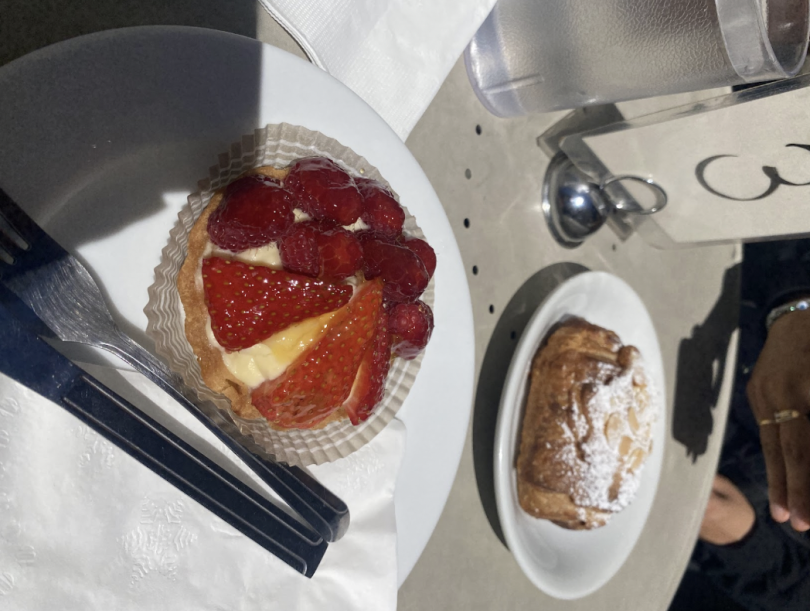 A fruit tart topped with fresh strawberries and raspberries beside a powdered almond croissant on a table set for dessert.