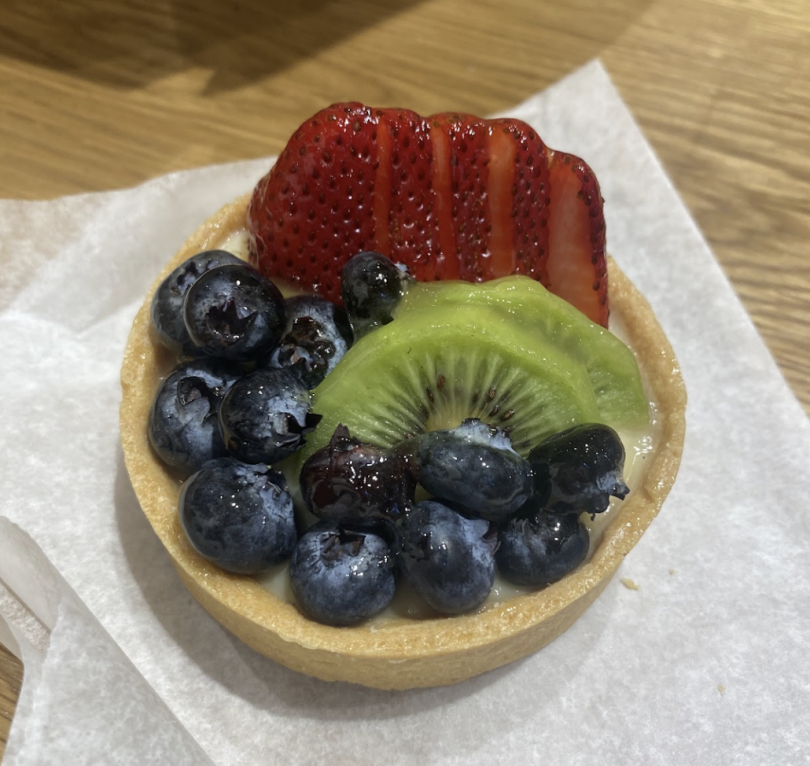 A small fruit tart topped with fresh strawberries, kiwi slices, and glossy blueberries on a crisp pastry base.