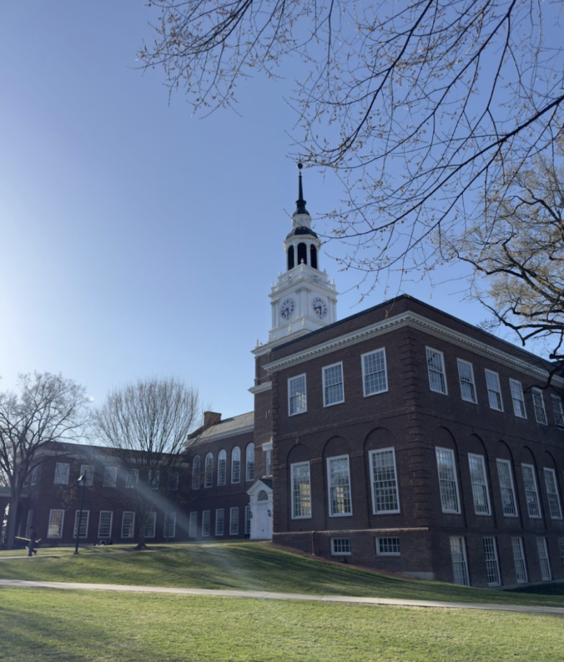 Baker-Berry Library at Dartmouth. The picture features the library on a bright blue sky day. Several students can be seen walking by the Baker-Berry Library.