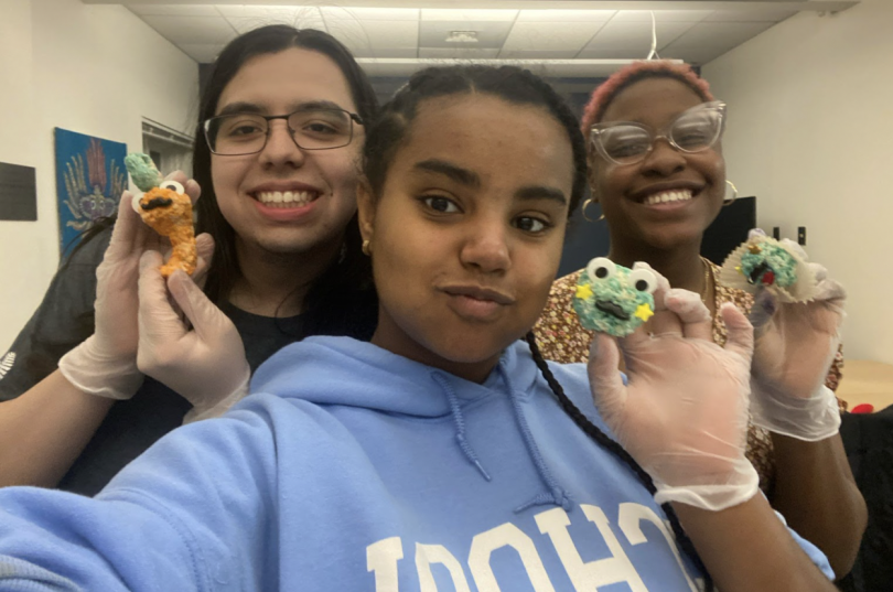 Amen, center of frame, has two friends on either side of her. They are all holding Rice Krispies treats and smiling for the camera.